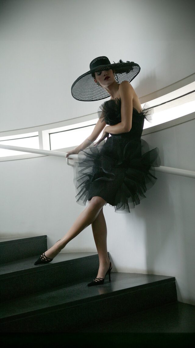 Vestido de cóctel de tafetán negro con detalles de panal y apliques de crin que forman los volantes. Pamela de rafia y crin negra. #manuelpertegaz